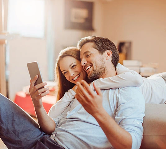 Happy Couple On Couch Using Phone